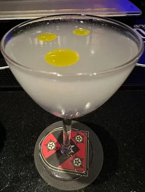 Martini glass with opaque drink and yellow drops on a patterned coaster.