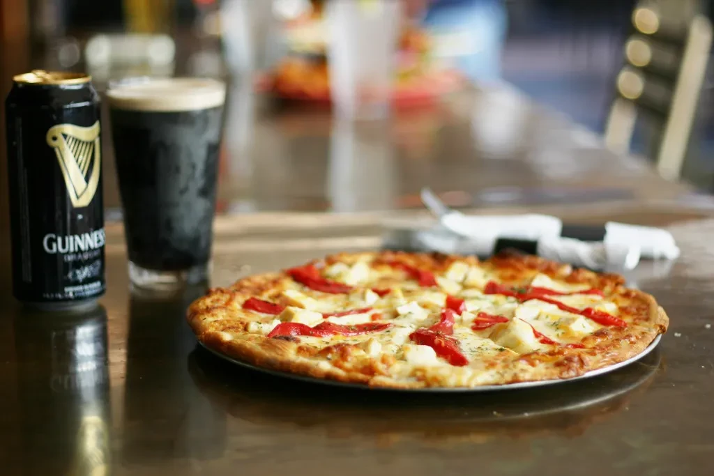 Pizza with peppers and cheese, beside Guinness beer can and stout.