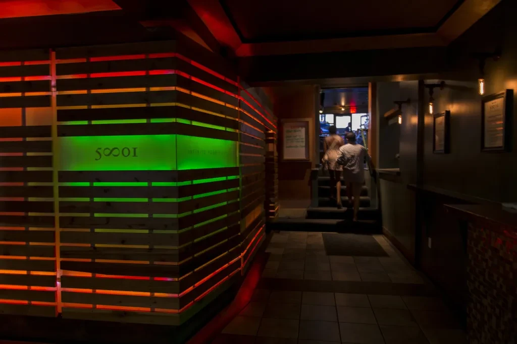 Modern restaurant hallway with colorful LED-lit wooden slat wall and people.
