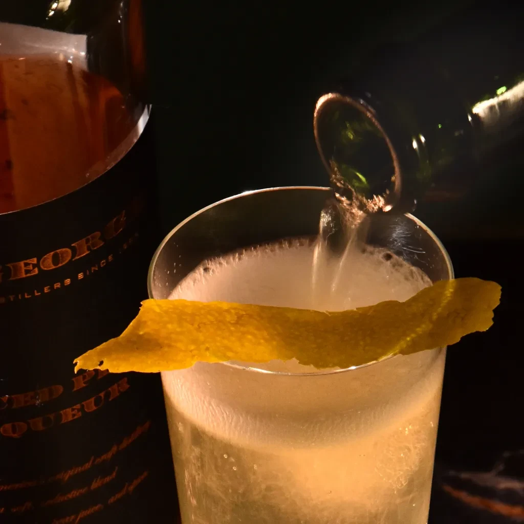 Sparkling cocktail with lemon peel being poured into a glass.