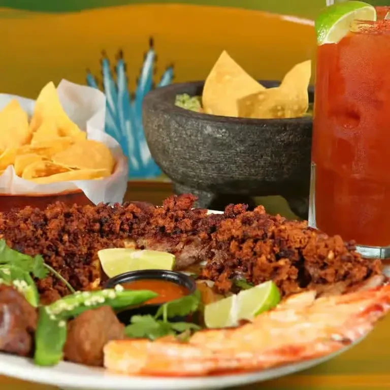 Colorful Mexican food spread: crumbled meat, shrimp, guacamole, chips, drink.