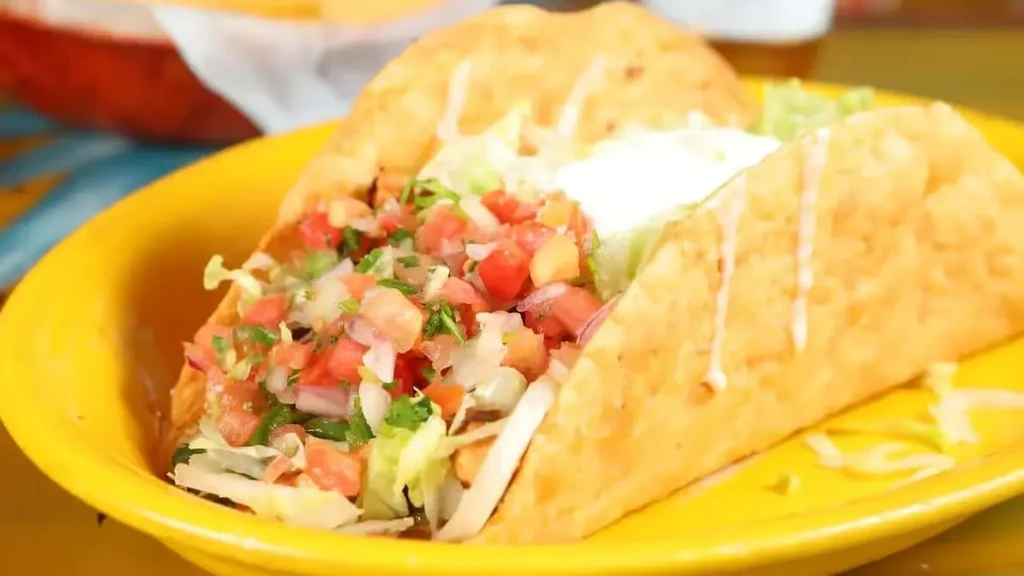 Crispy hard-shell taco on yellow plate, filled with lettuce, pico, sour cream.