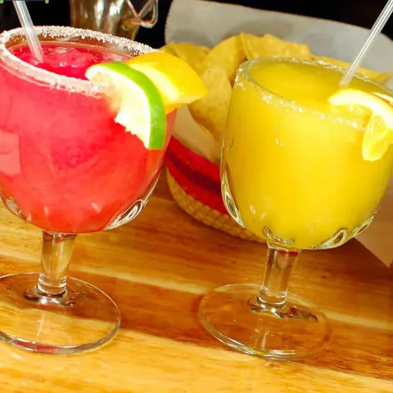 Frozen red and yellow margaritas in salt-rimmed glasses on a table.