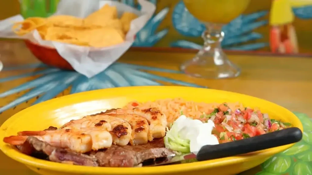 Grilled steak and shrimp dinner with sides on a bright yellow plate.