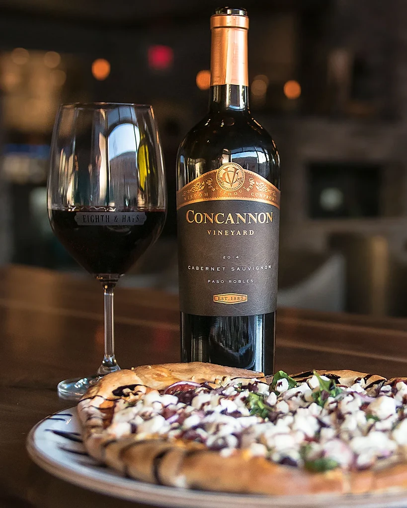 Concannon Cabernet Sauvignon wine bottle, wine glass, and blurred gourmet pizza.