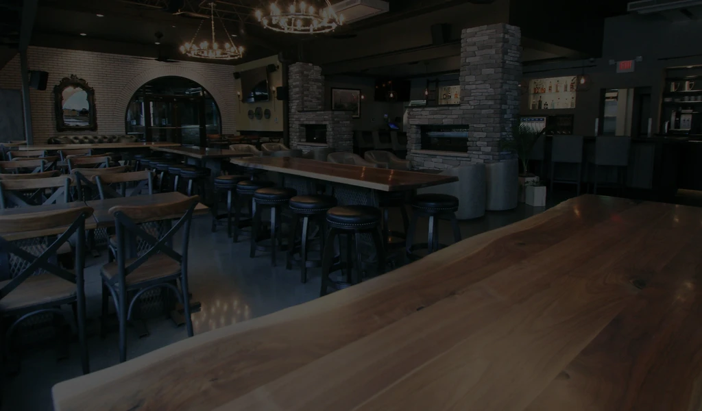 Dimly lit, empty restaurant interior: live-edge tables, bar, and chandeliers.