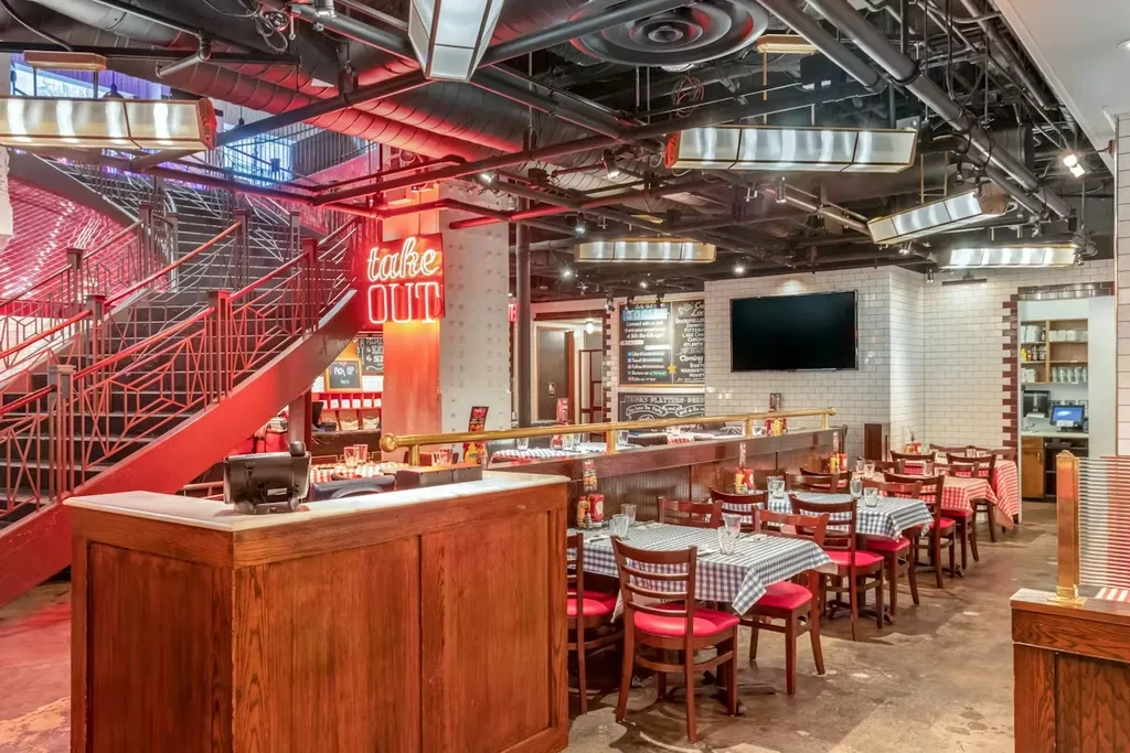 Industrial-chic restaurant with a red staircase, checkered tables, and "take OUT" sign.