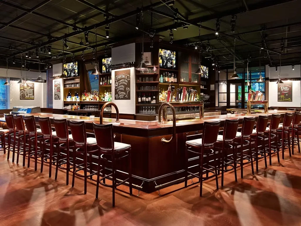 Empty modern bar with U-shaped counter, stools, liquor, and TVs.