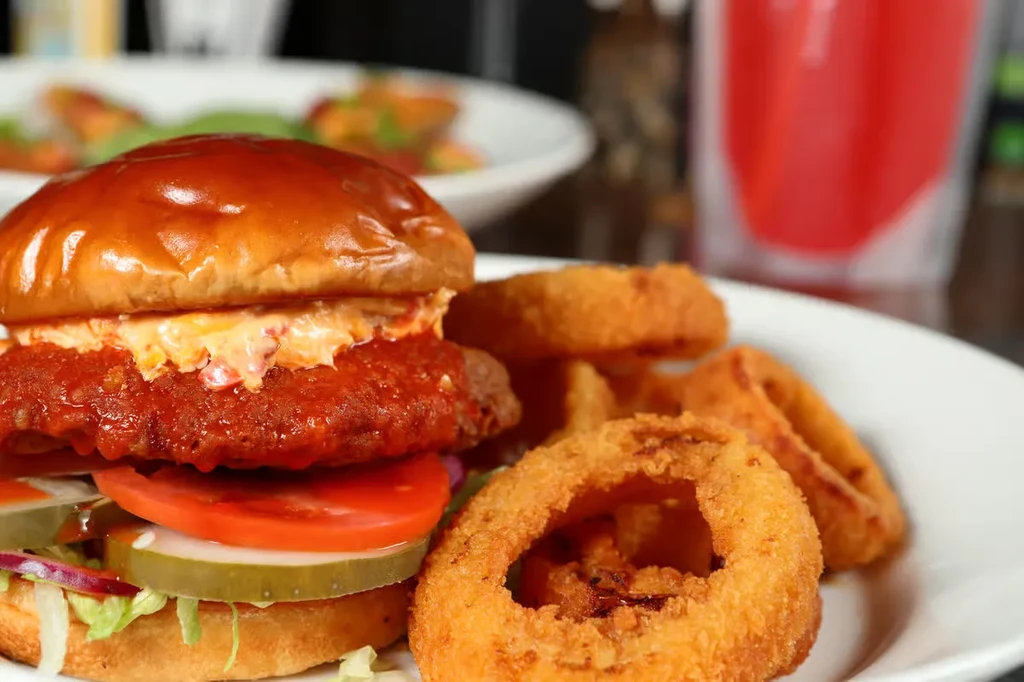 Burger with lettuce, tomato, pickles, and crispy golden onion rings.