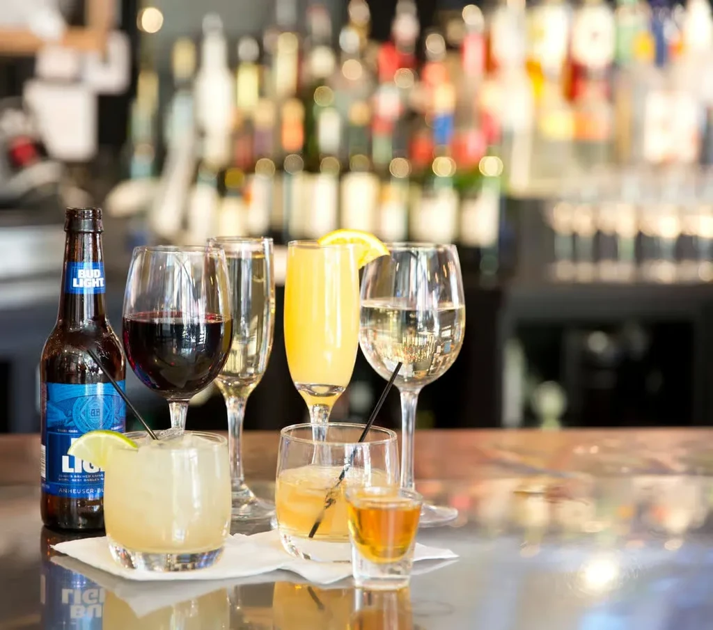 Various alcoholic drinks on a reflective bar counter with blurred bottles.