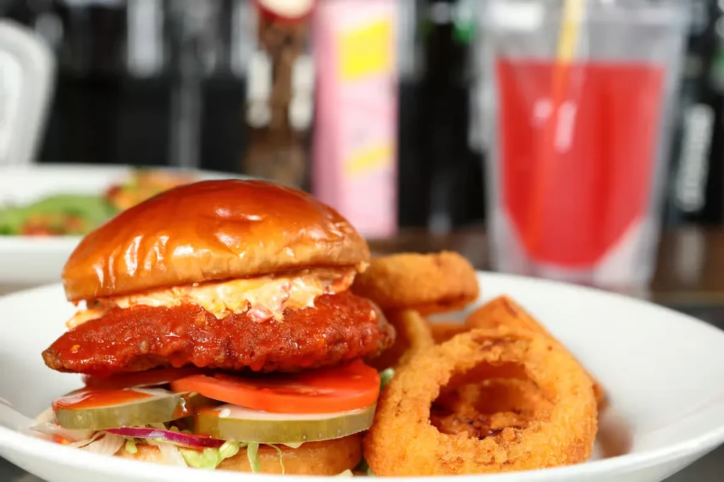 Large chicken burger and golden onion rings on a white plate.