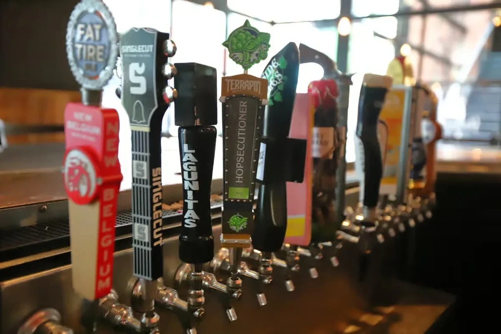 Close-up of colorful beer tap handles from various brands in a bar.