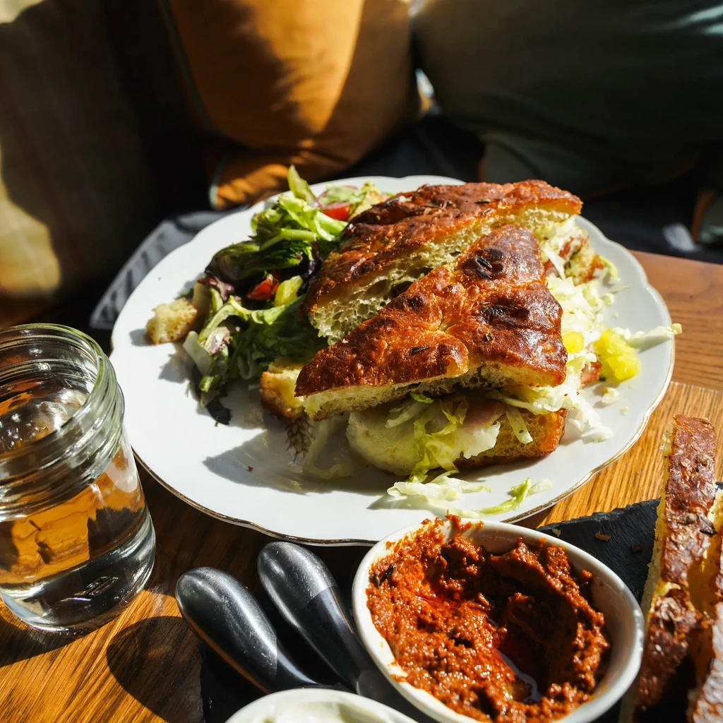 Focaccia sandwich, green salad, dips, and water on a wooden table.
