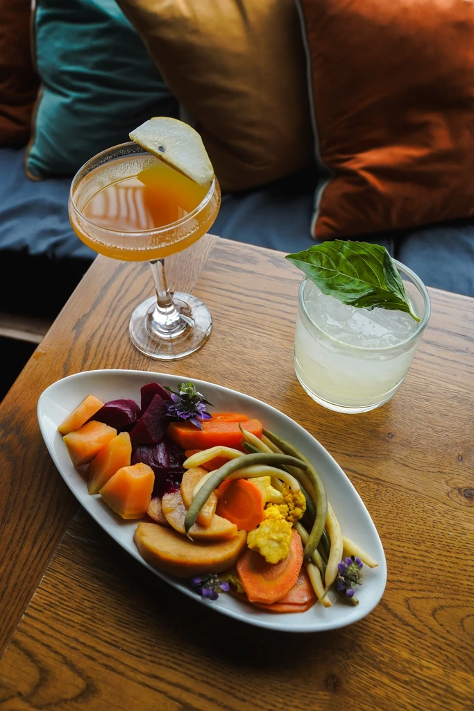 Colorful vegetable plate and two garnished cocktails in a restaurant setting.