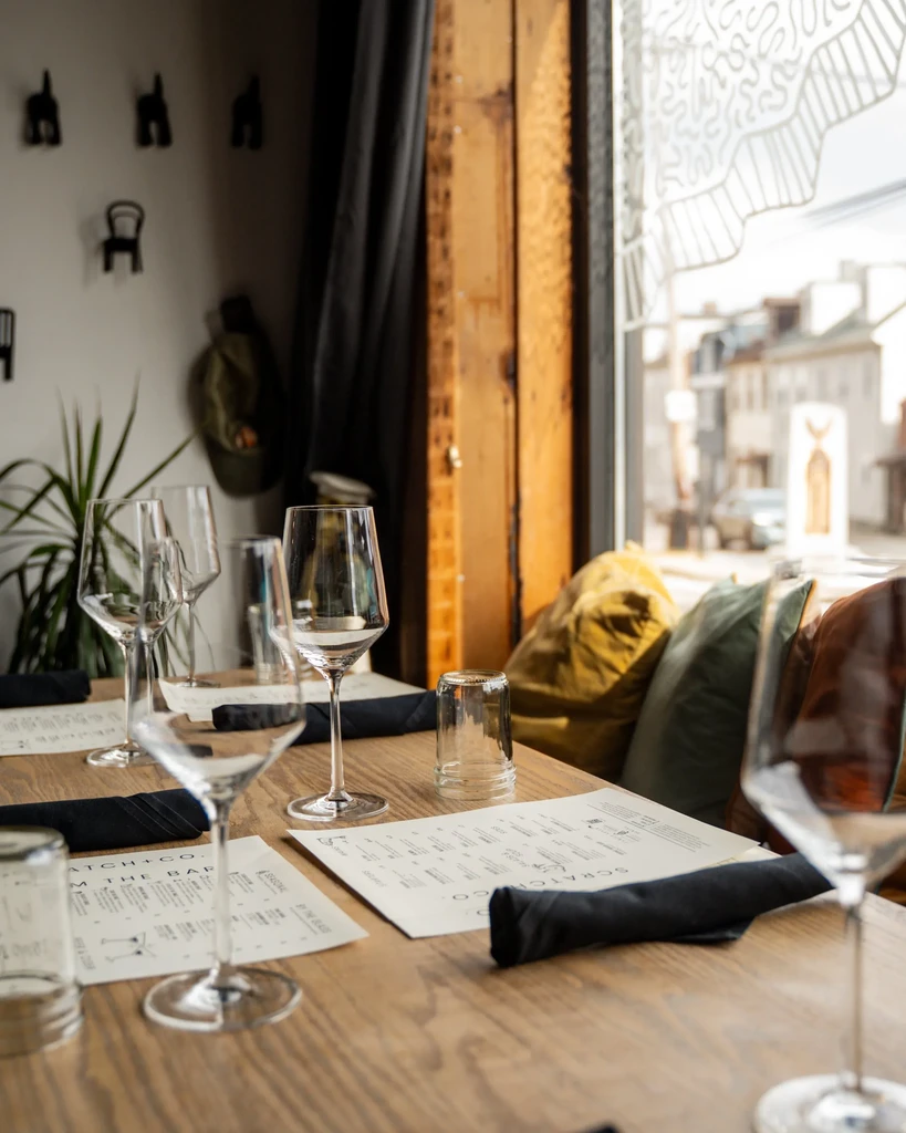 Bright restaurant table set with modern glasses, menus; street view outside.