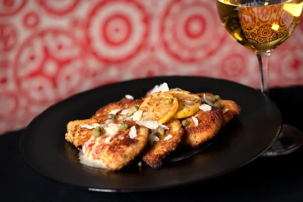 Breaded cutlet topped with lemon, capers, parmesan, beside white wine.