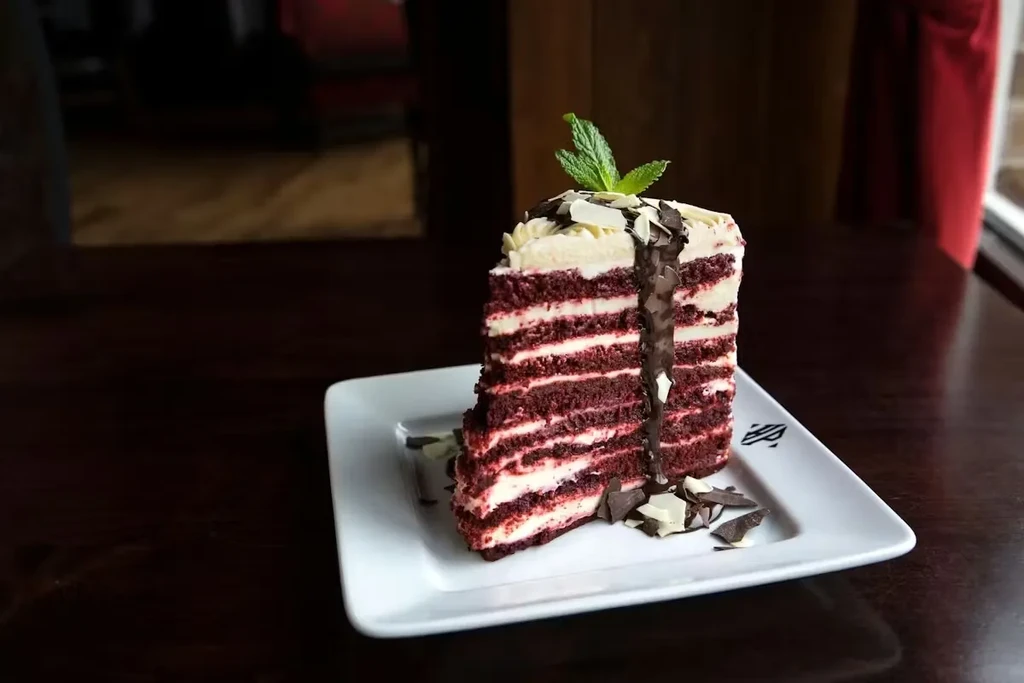 Layered red velvet cake slice with cream cheese frosting, chocolate, mint.