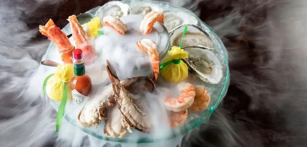 Seafood tower with crab, shrimp, lobster, oysters, and dry ice smoke.