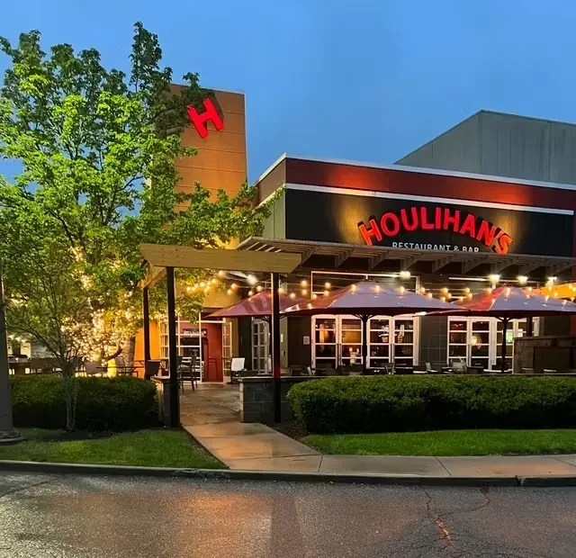 Houlihan's restaurant exterior at dusk, illuminated sign, patio, wet ground.