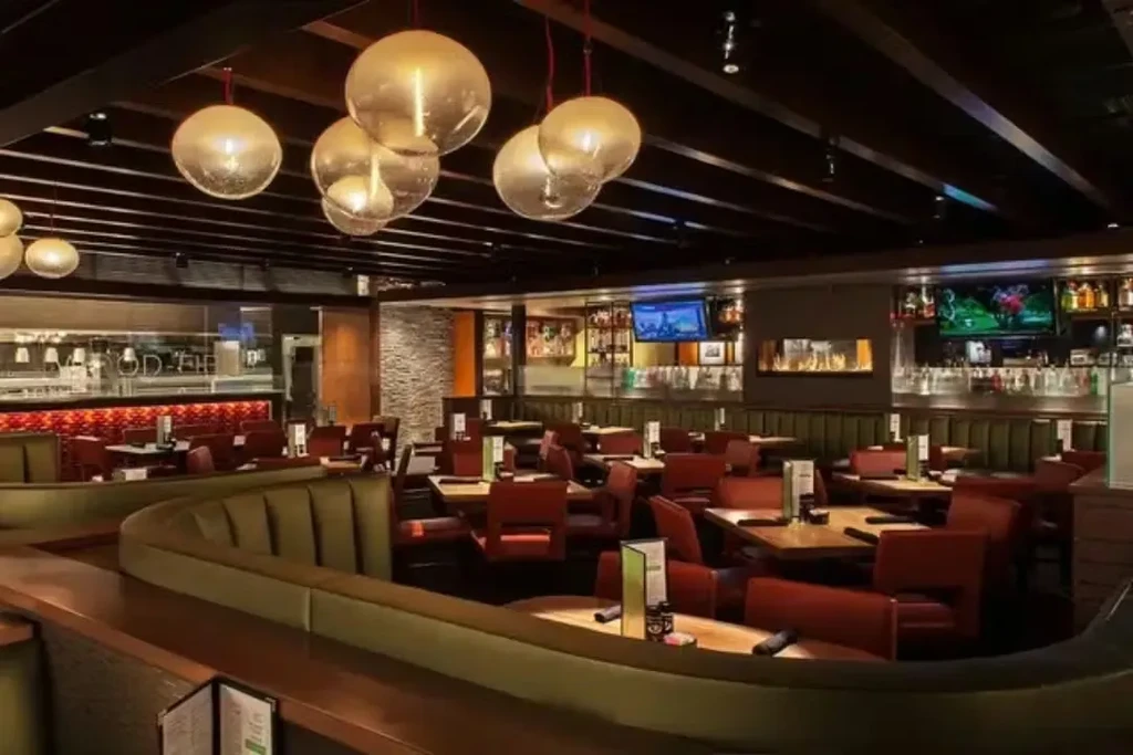 Empty modern restaurant with olive booths, bar, fireplace, and sports TVs.
