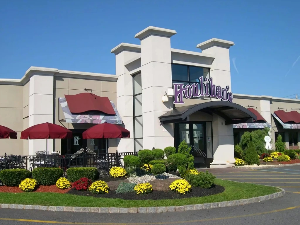 Modern Houlihan's restaurant exterior with patio, red umbrellas, and colorful landscaping.