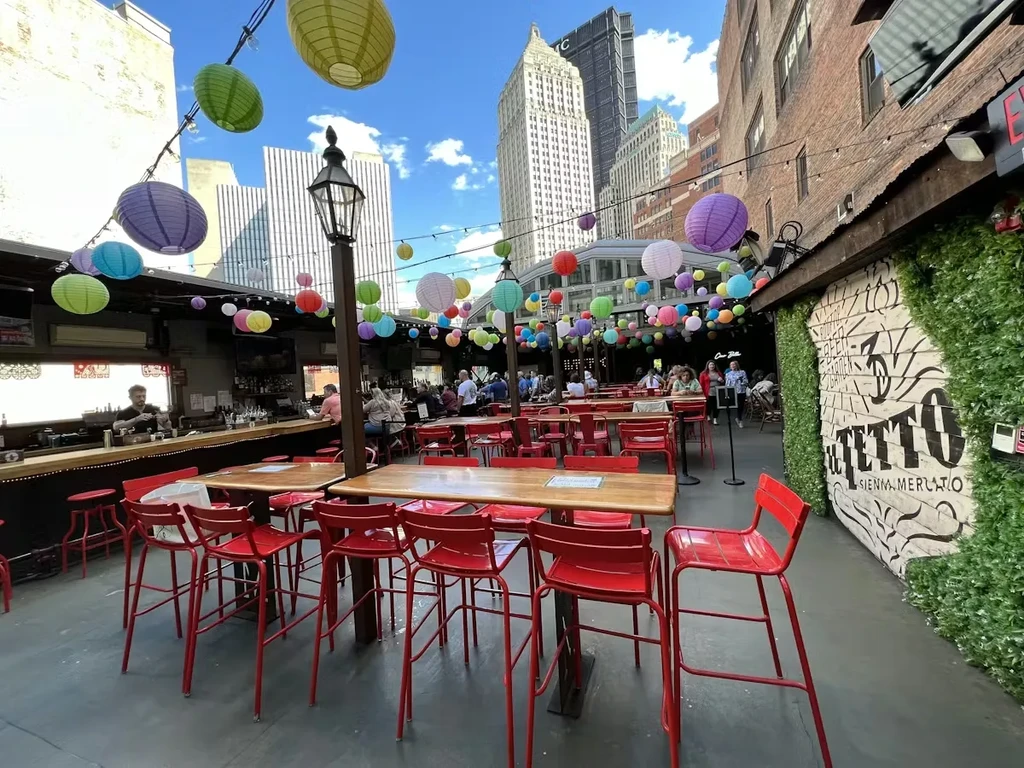 Vibrant rooftop bar patio with colorful lanterns, diners, and urban skyline.