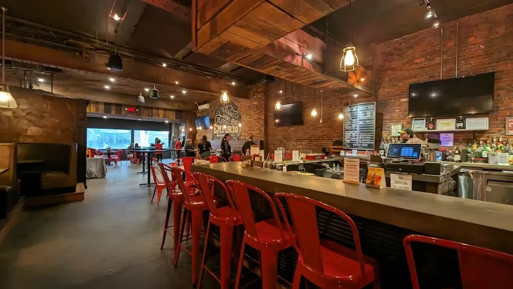 Industrial-rustic interior featuring red bar stools, brick walls, and warm light.