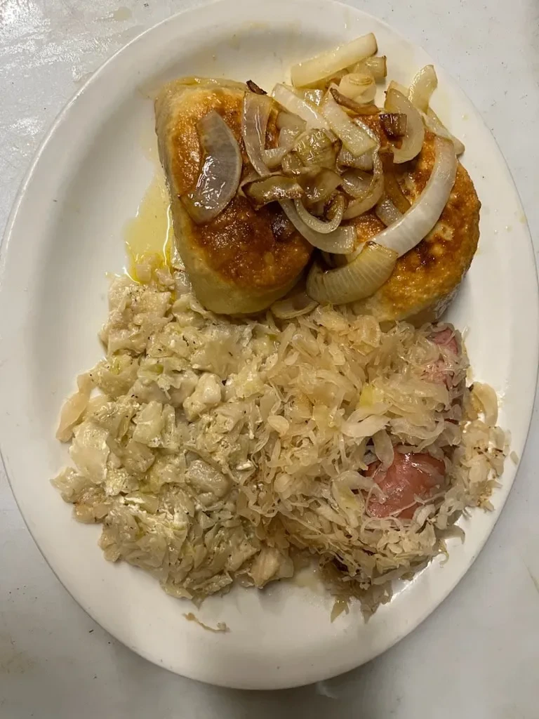Golden-brown fried items, onions, sauerkraut, and sausage on oval plate.