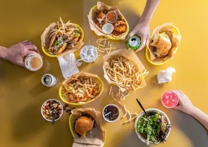 Hands share a casual meal of fries, burgers, salad, and drinks.