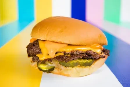 Double cheeseburger, melted cheese, pickles, onions, vibrant abstract background.