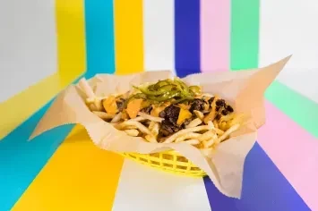 Loaded french fries in yellow basket with cheese, meat, and peppers.