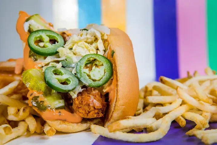 Fried chicken sandwich with jalapeños, pickles, sauce, and french fries.
