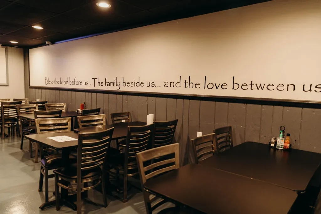Empty restaurant dining area with dark tables, chairs, and family quote.