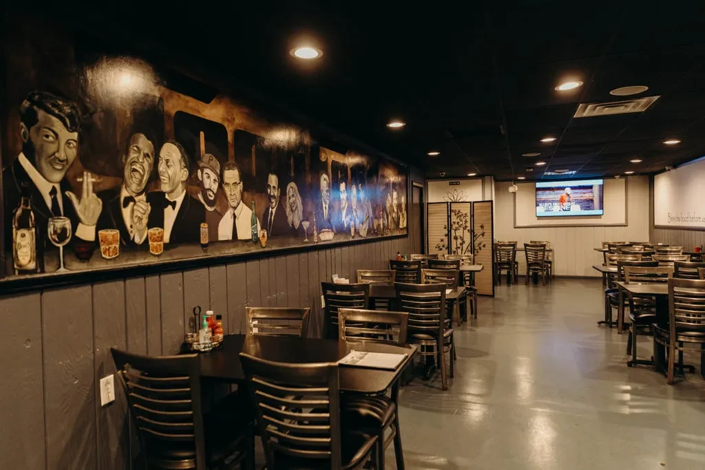 Restaurant dining room with a vibrant Rat Pack mural and dim lighting.