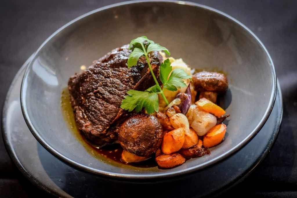 Artfully plated braised beef, mashed potatoes, roasted vegetables, and parsley.