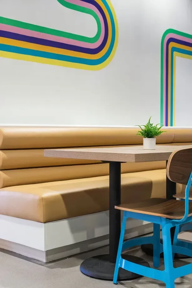 Bright cafe interior: camel booth, wooden table, turquoise chair, retro wall.