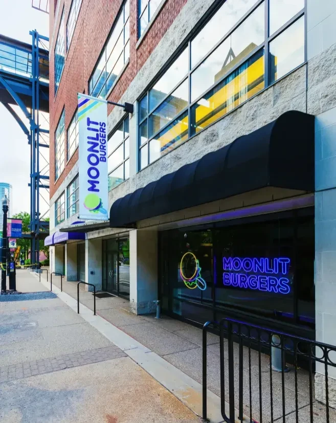 Moonlit Burgers restaurant exterior: modern stone and brick building with neon sign.