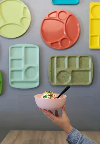 Hand in denim holds pink ice cream with sprinkles, colorful wall plates.