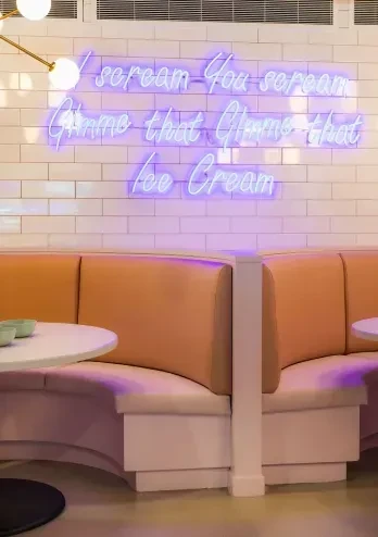 Modern ice cream parlor with peach booths and purple neon ice cream sign.