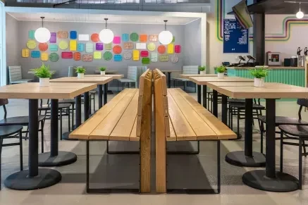 Modern restaurant interior with light-wood furniture and colorful mosaic wall art.