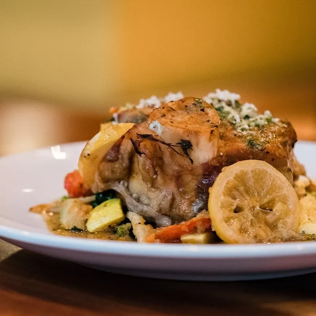 Braised meat shank with vegetables, lemon, and savory sauce.