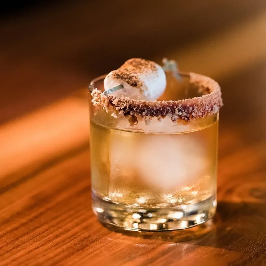 Amber cocktail with spherical ice, granular rim, and marshmallow garnish.