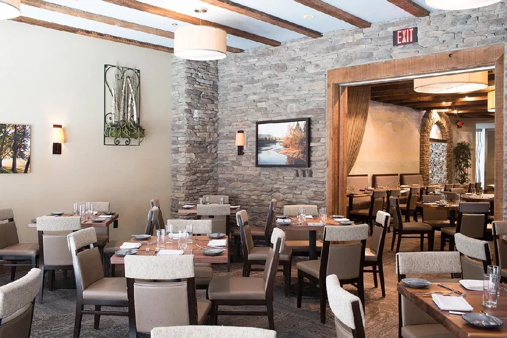 Restaurant dining room with stone walls, exposed beams, and set tables.