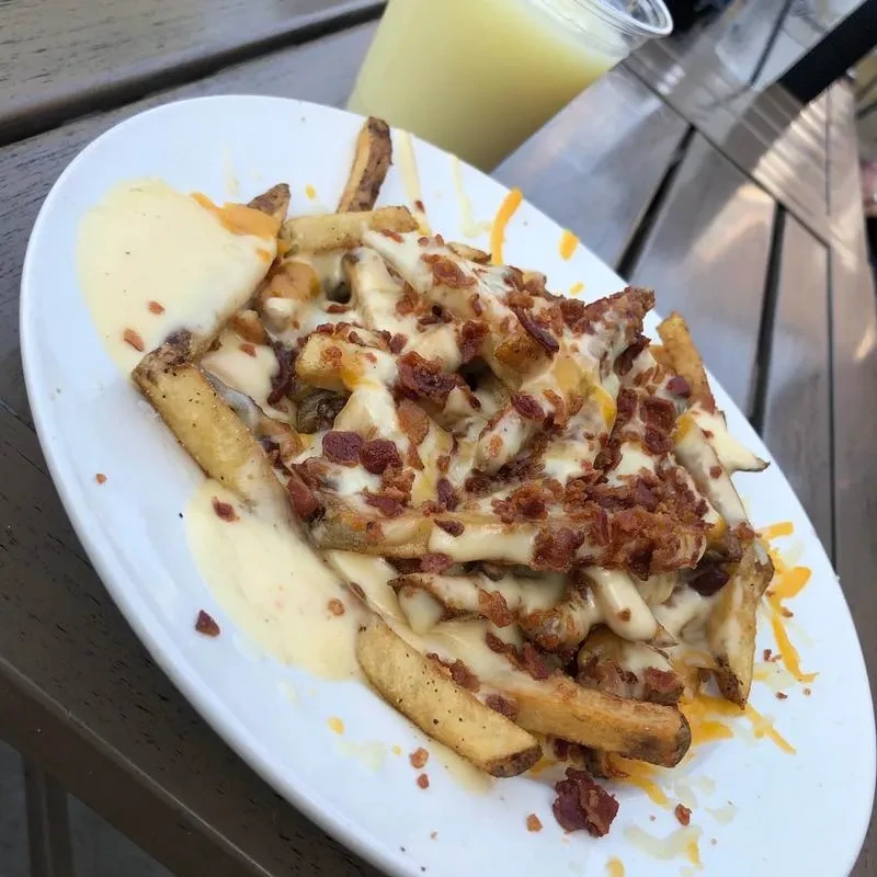 Oval plate of thick-cut fries topped with melted cheese and bacon.
