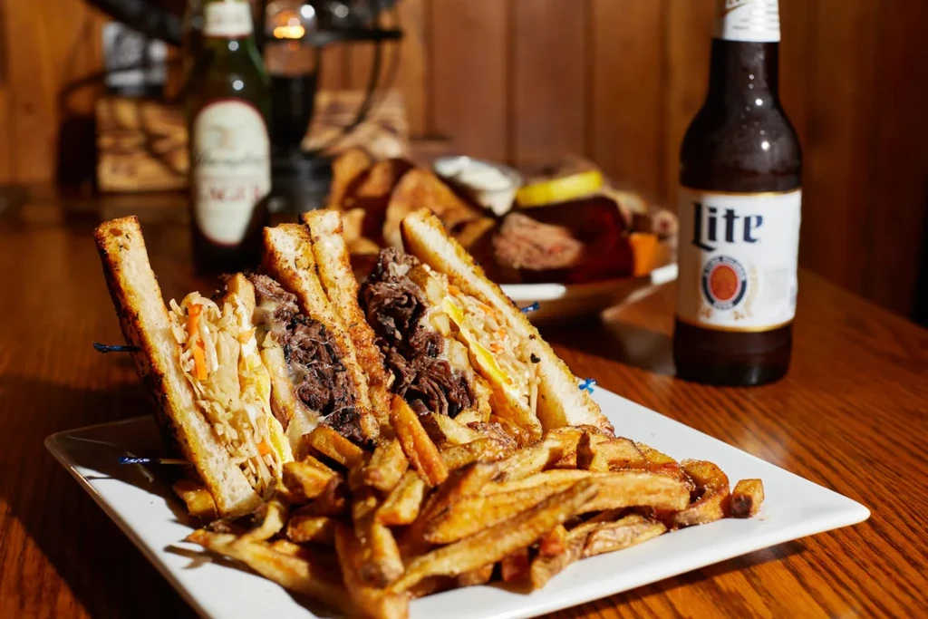 A large shredded meat sandwich, fries, and Miller Lite on wood.
