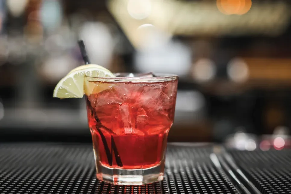 Vibrant red cocktail in faceted glass with ice, straw, and lime.