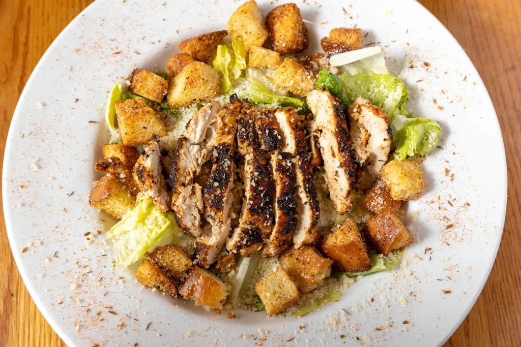Close-up of grilled chicken Caesar salad with croutons and cheese.