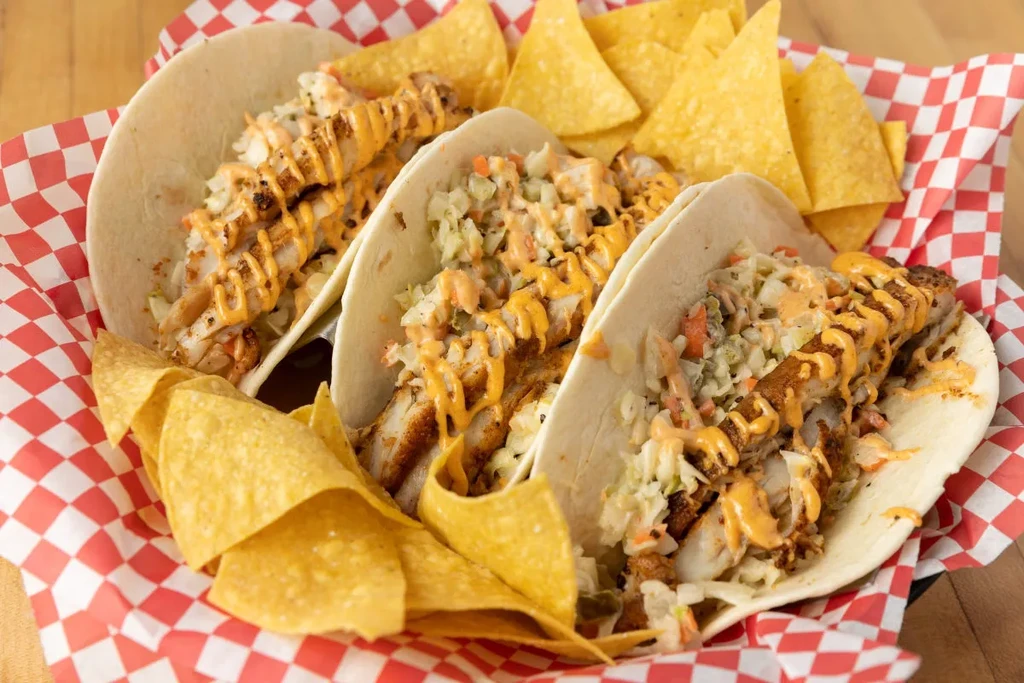Three tacos with coleslaw, sauce, and chips in a rustic basket.