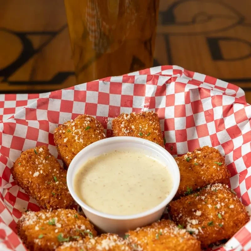 Golden fried food with cheese and herbs, dipping sauce, in a checkered basket.