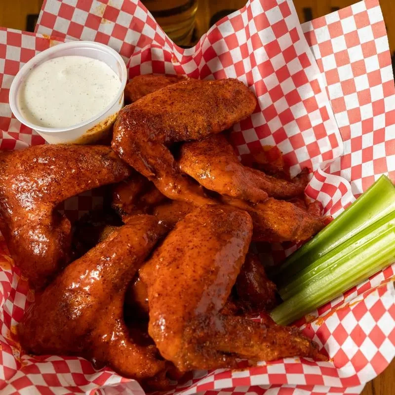 Cooked chicken wings with reddish-orange sauce, white dip, and celery.